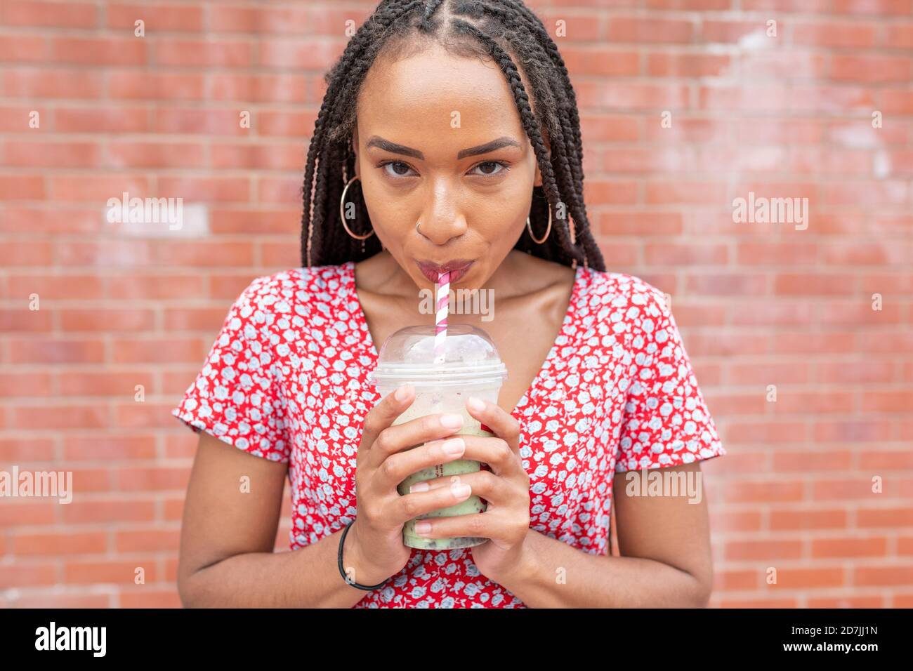 Jeune femme buvant du smoothie en se tenant contre le mur Banque D'Images
