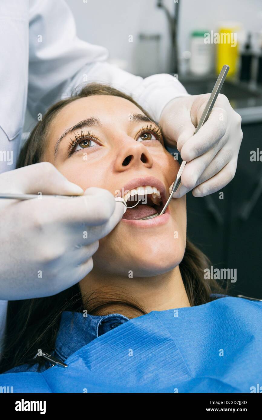 Dentiste en gants examinant la cavité buccale de joli patient à clinique Banque D'Images