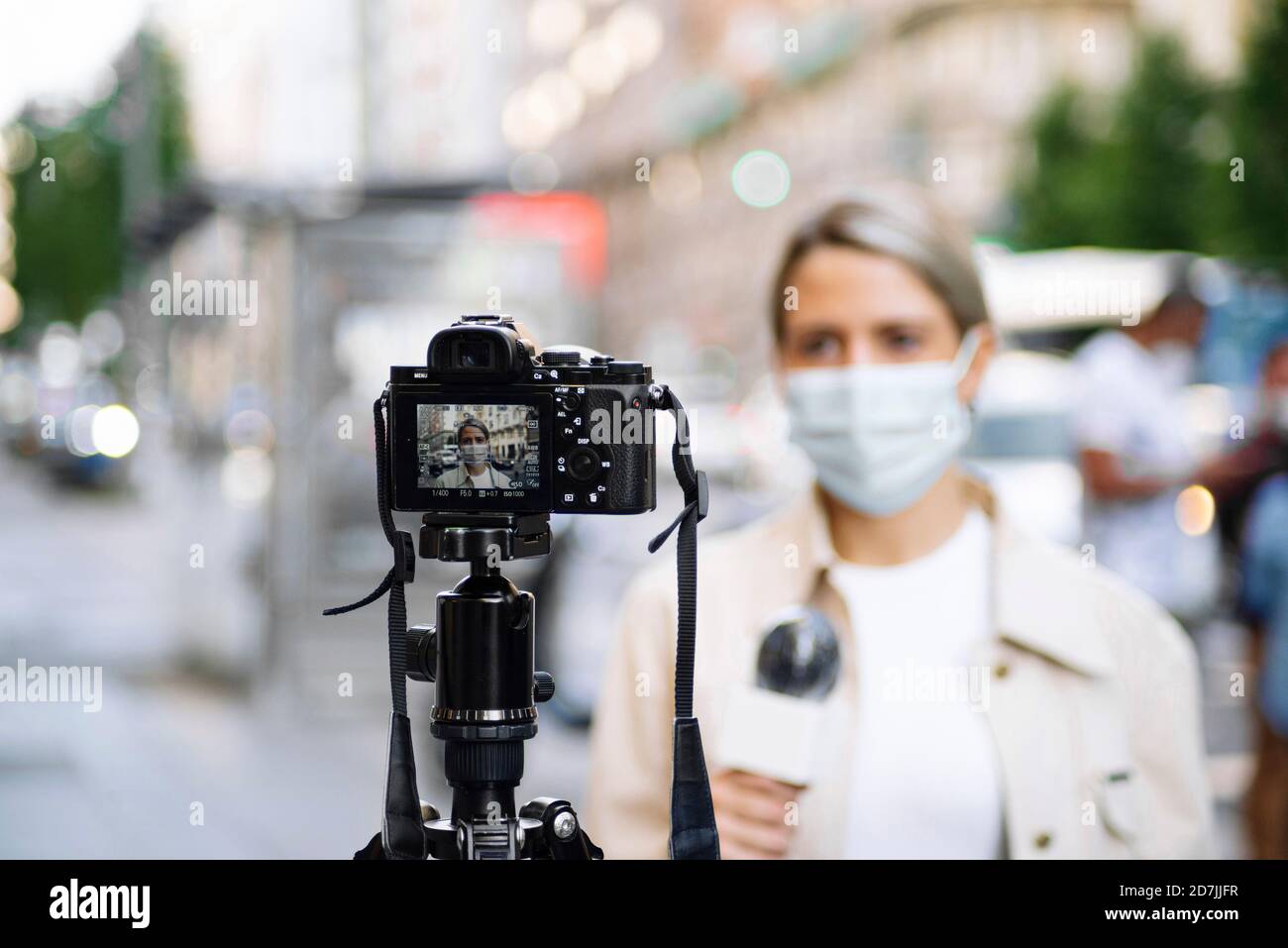 Femme journaliste portant un masque filmant avec un appareil photo en ville Banque D'Images