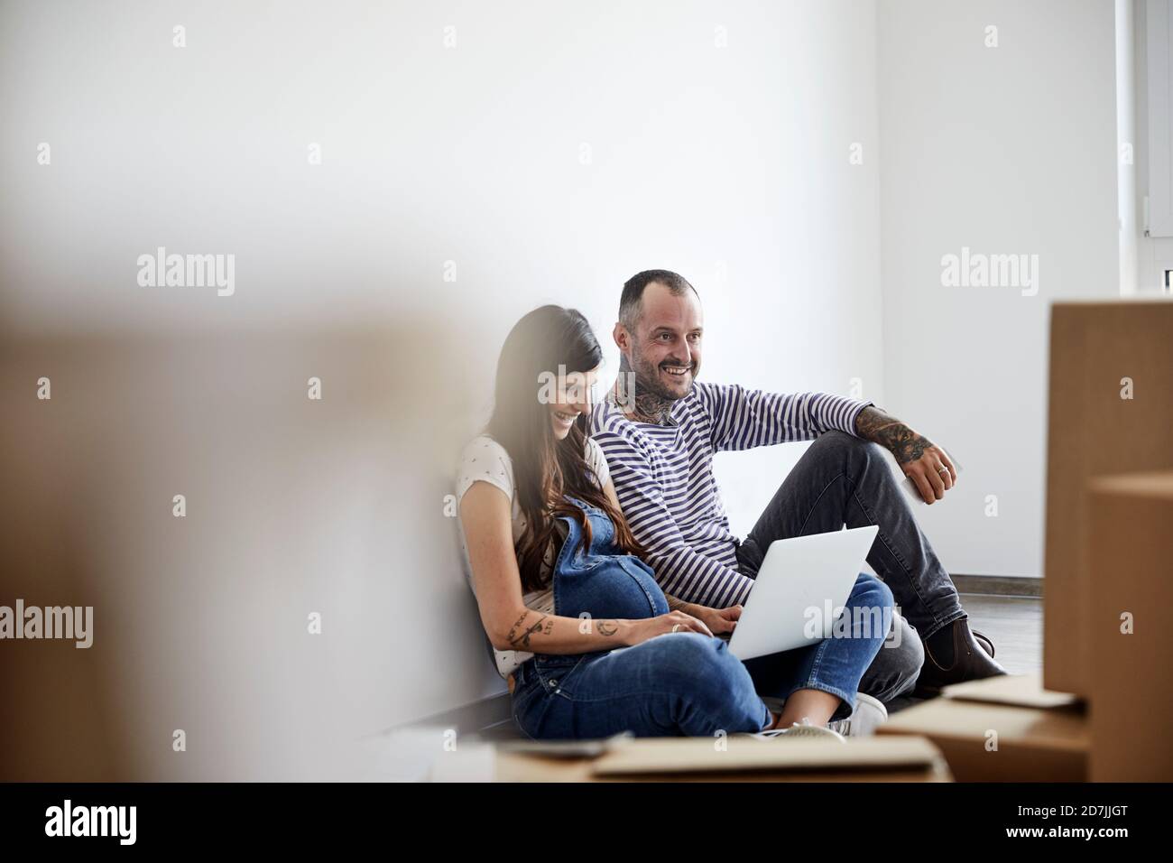 Couple heureux travaillant sur ordinateur portable tout en étant assis dans la chambre Banque D'Images