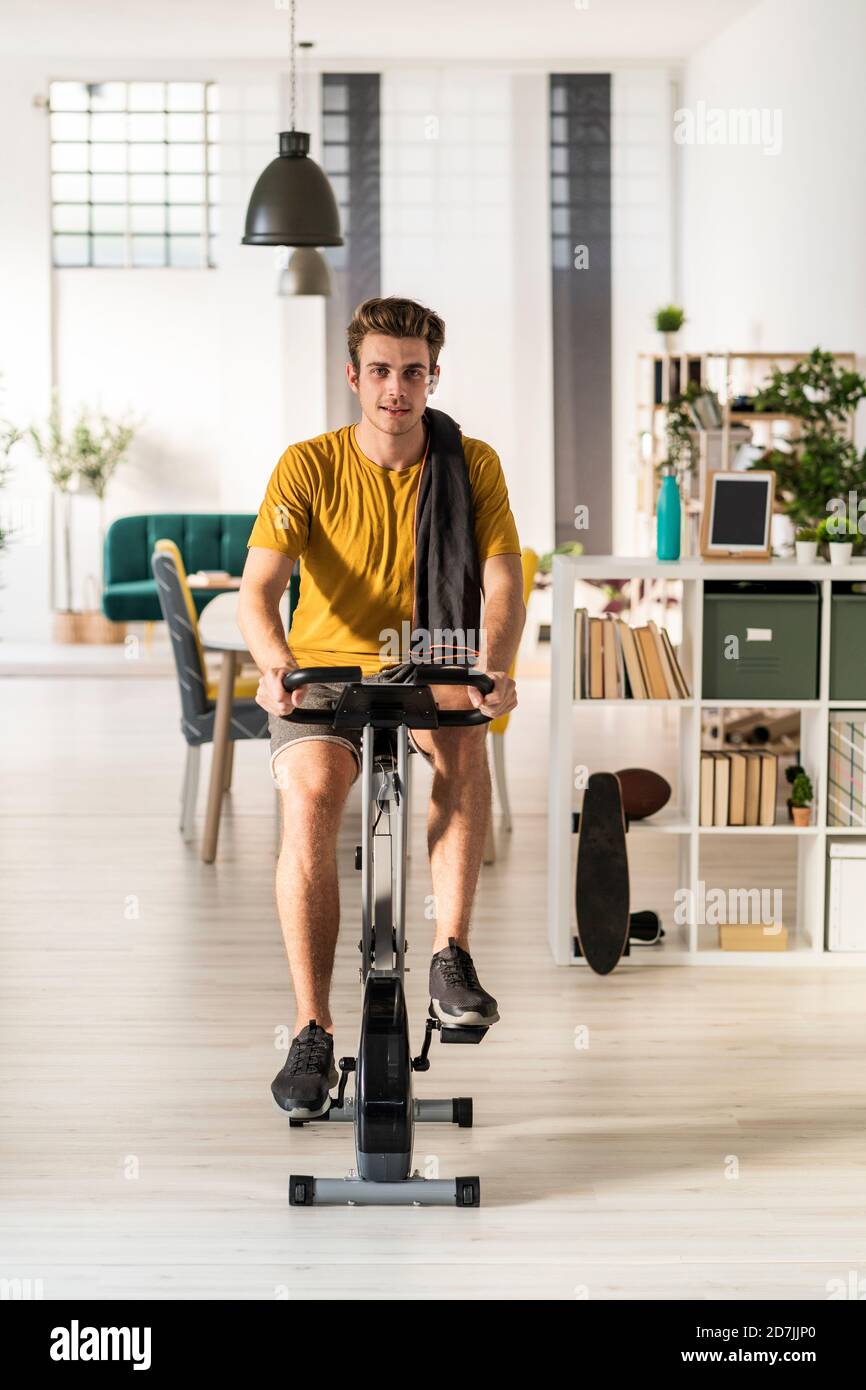 Jeune homme à vélo sur l'équipement d'exercice à la maison Banque D'Images