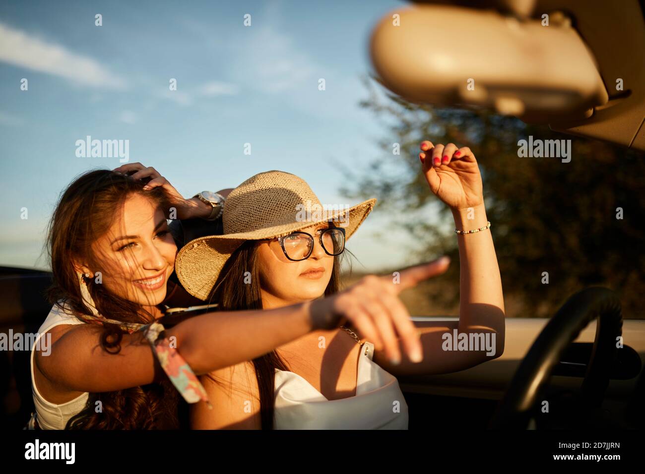 Des jeunes amis souriants se mettent à pointer en étant assis dans une voiture convertible Banque D'Images