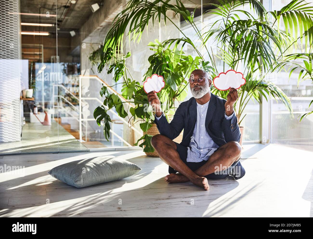 Contemplant un homme tenant une bulle de pensée tout en étant assis avec une jambe croisée à la maison Banque D'Images