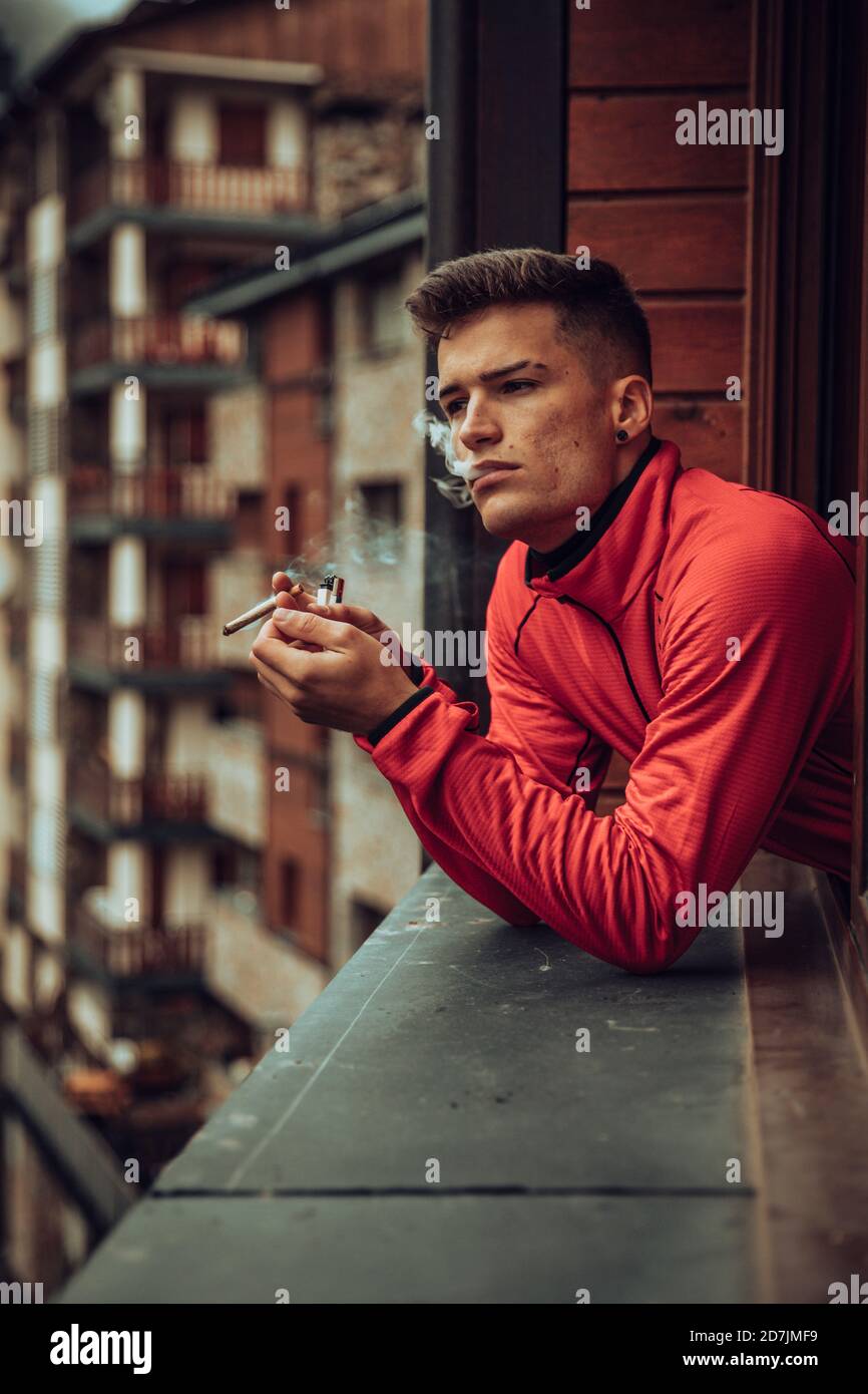 Un jeune homme fume du joint de marijuana tout en regardant par la fenêtre Banque D'Images