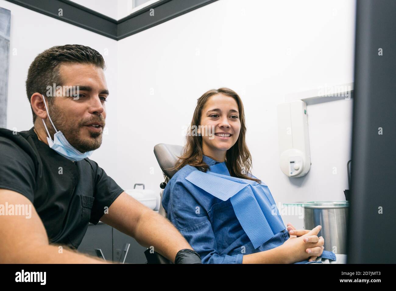 Beau dentiste masculin expliquant la procédure médicale à la patiente souriante sur ordinateur portable dans la clinique Banque D'Images