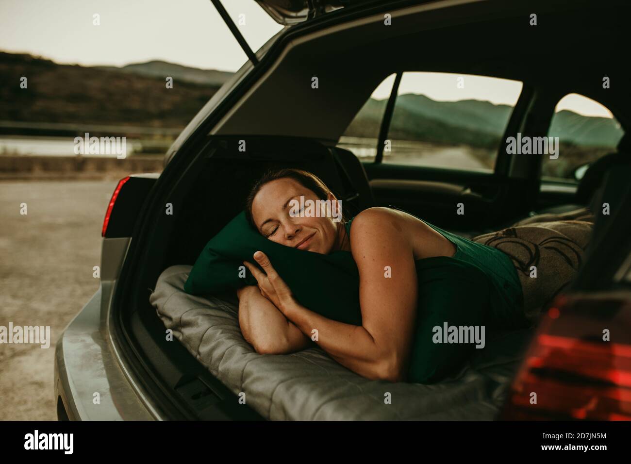 Femme fatiguée dormant dans un coffre de voiture confortable au crépuscule Banque D'Images