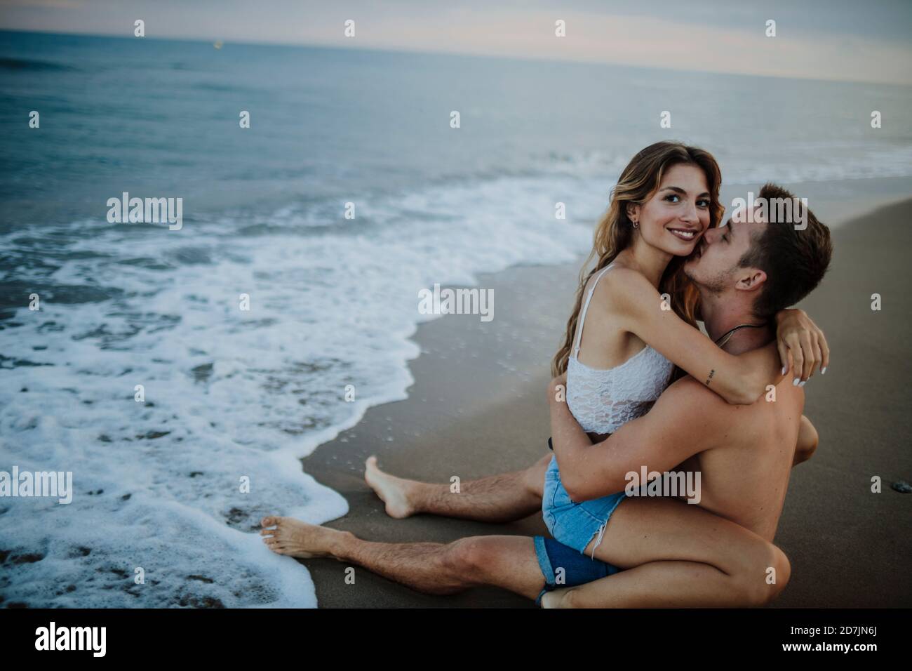 Homme embrassant femme assis sur ses genoux à la plage Banque D'Images
