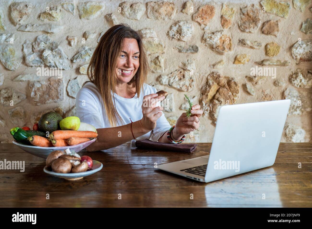 Une femme mature qui influence la nourriture vlogging tout en tenant le romarin et les champignons contre le mur de pierre Banque D'Images