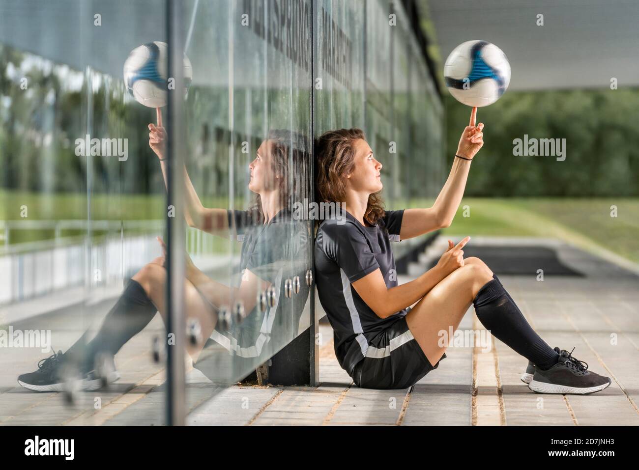 Une joueuse de football fait tourner la balle sur le doigt tout en étant assise paroi en verre Banque D'Images