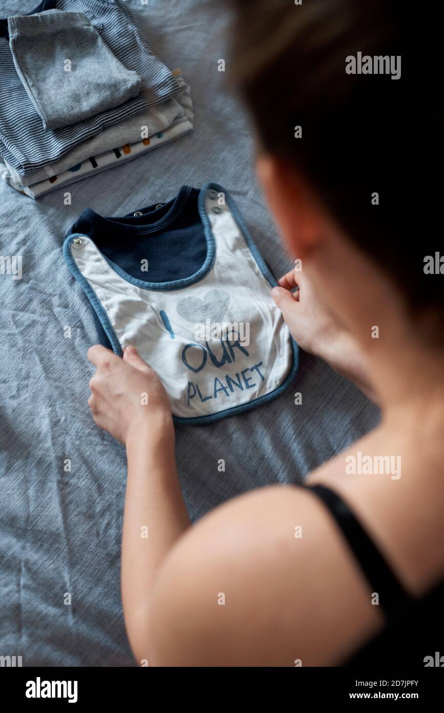 Femme enceinte pliant des vêtements de bébé sur le lit à la maison Banque D'Images