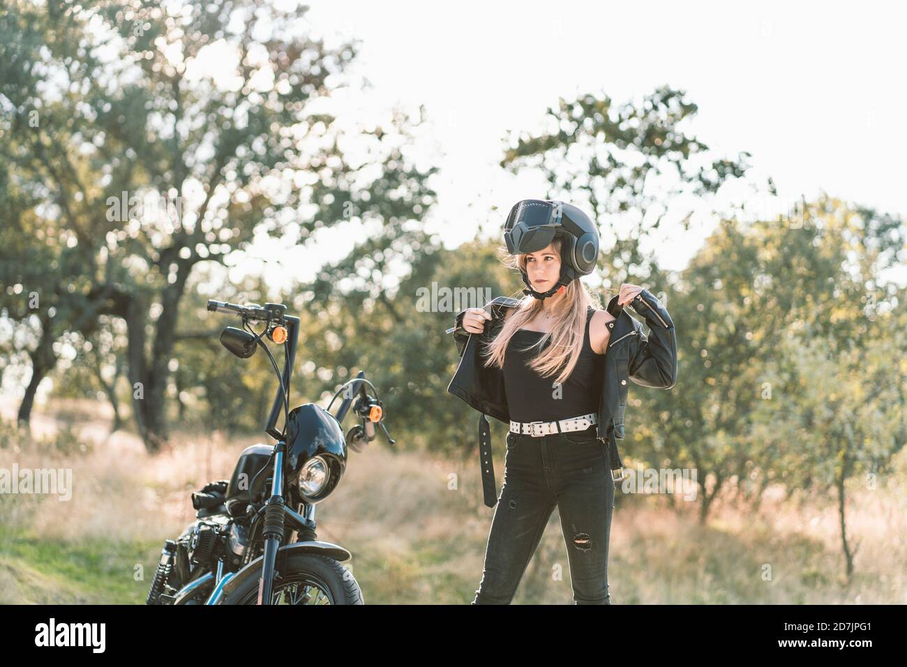 Blonde jeune femme motard vêtu d'une veste en cuir tout en restant debout moto Banque D'Images