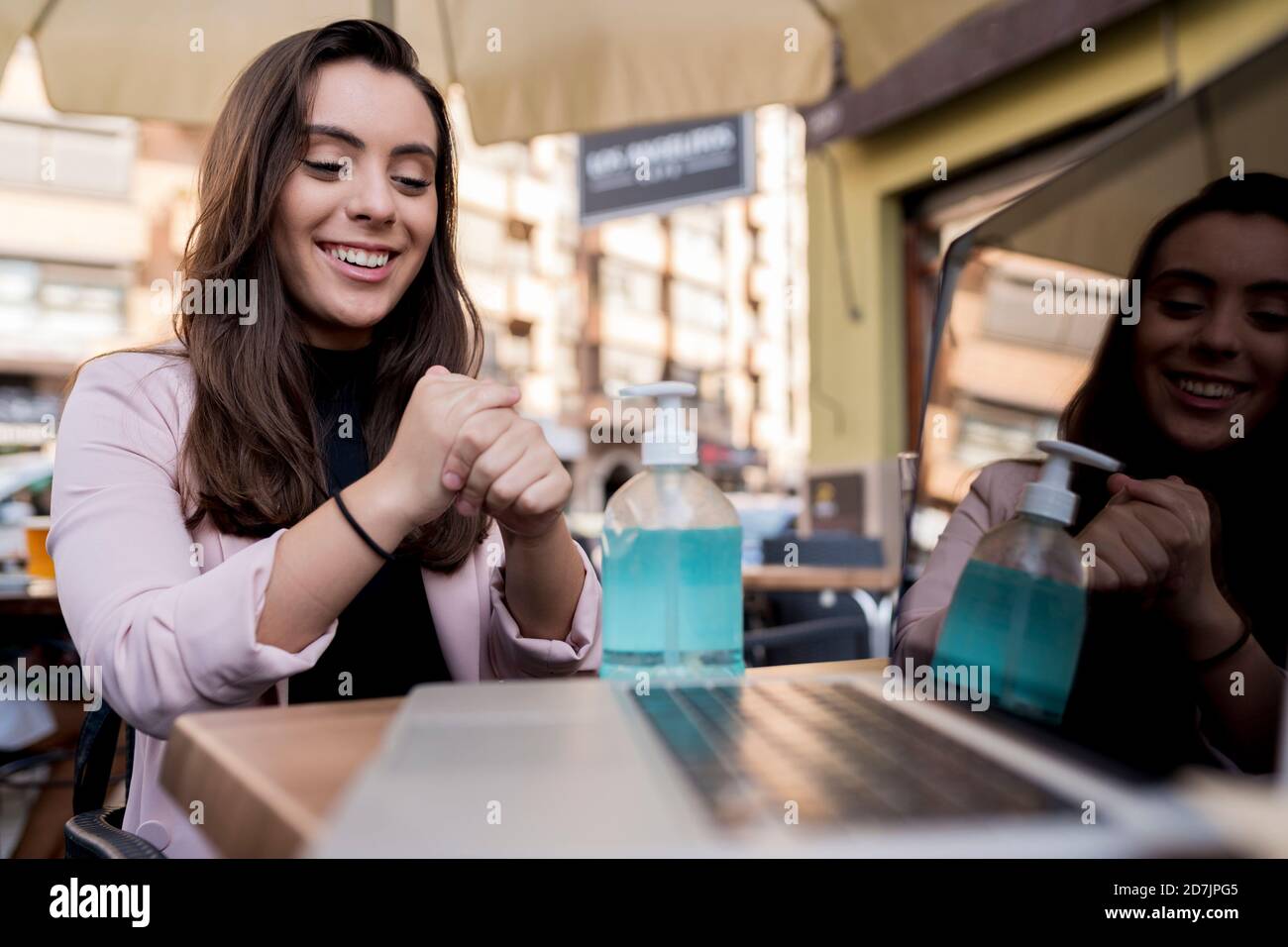 Jeune femme d'affaires souriante utilisant un désinfectant pour les mains dans un café pendant le COVID-19 épidémie Banque D'Images