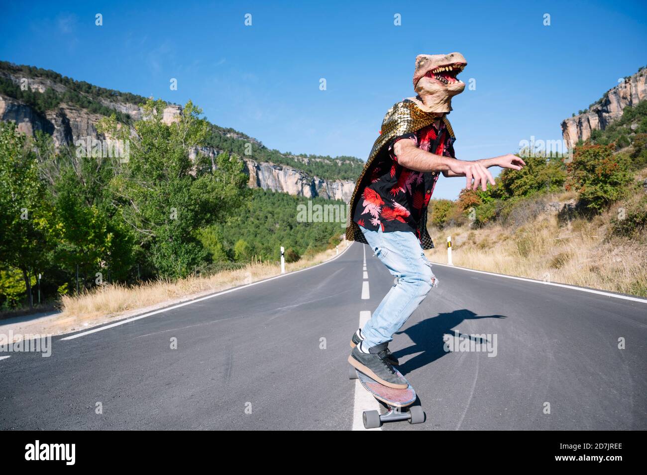Homme portant un masque de dinosaure skate sur la route contre un ciel dégagé Banque D'Images