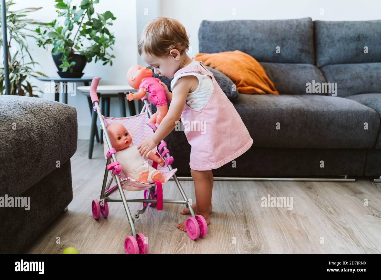Adorable petite fille mettant des jouets dans la poussette de bébé en position debout à la maison Banque D'Images