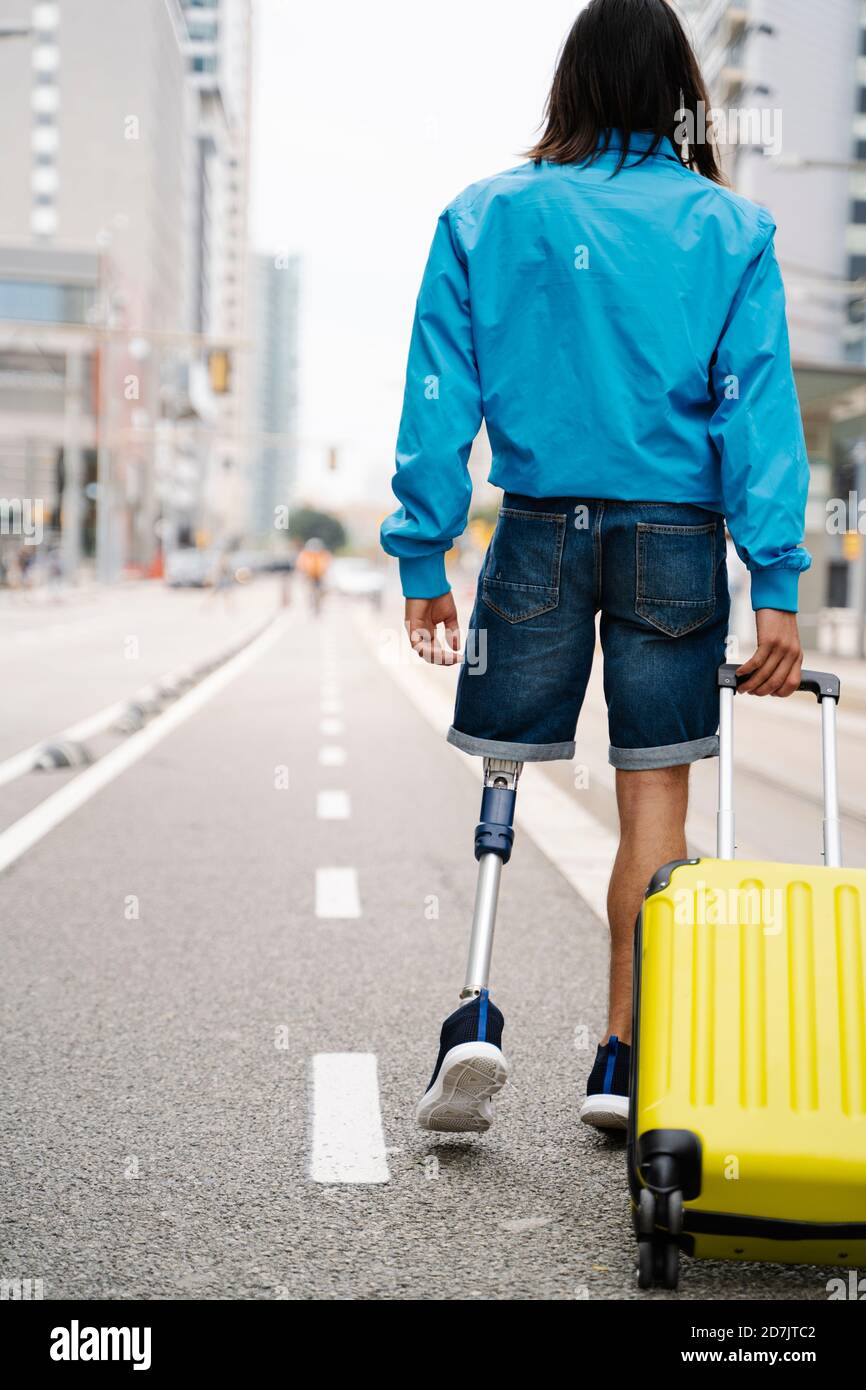 Jeune homme handicapé marchant avec des bagages sur la route dans la ville Banque D'Images