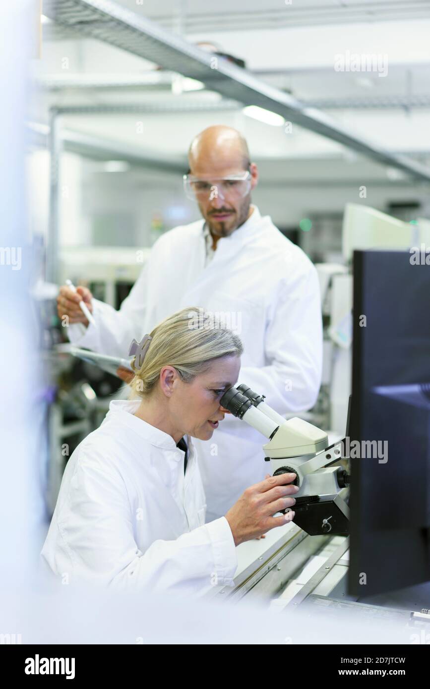 Scientifique féminin faisant de la recherche tout en regardant au microscope par homme collègue en laboratoire Banque D'Images