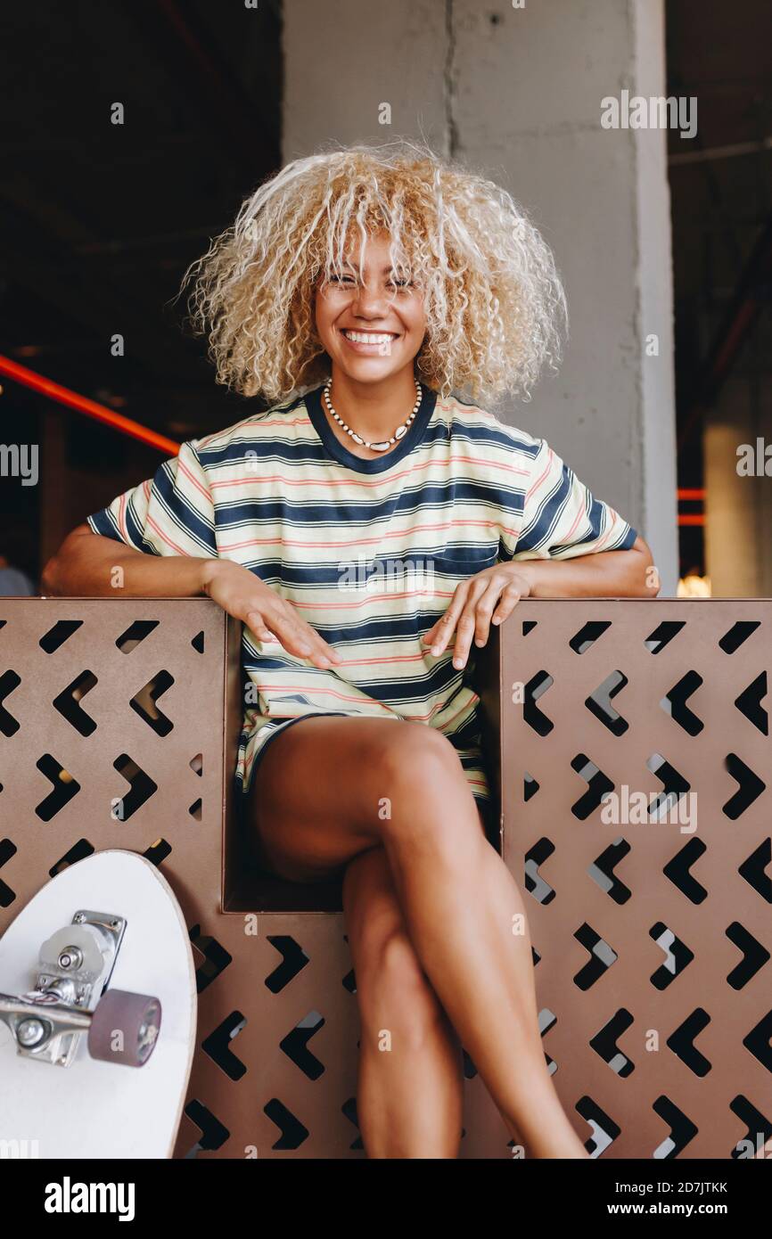 Blonde gaie Afro femme assise avec les jambes croisées Banque D'Images