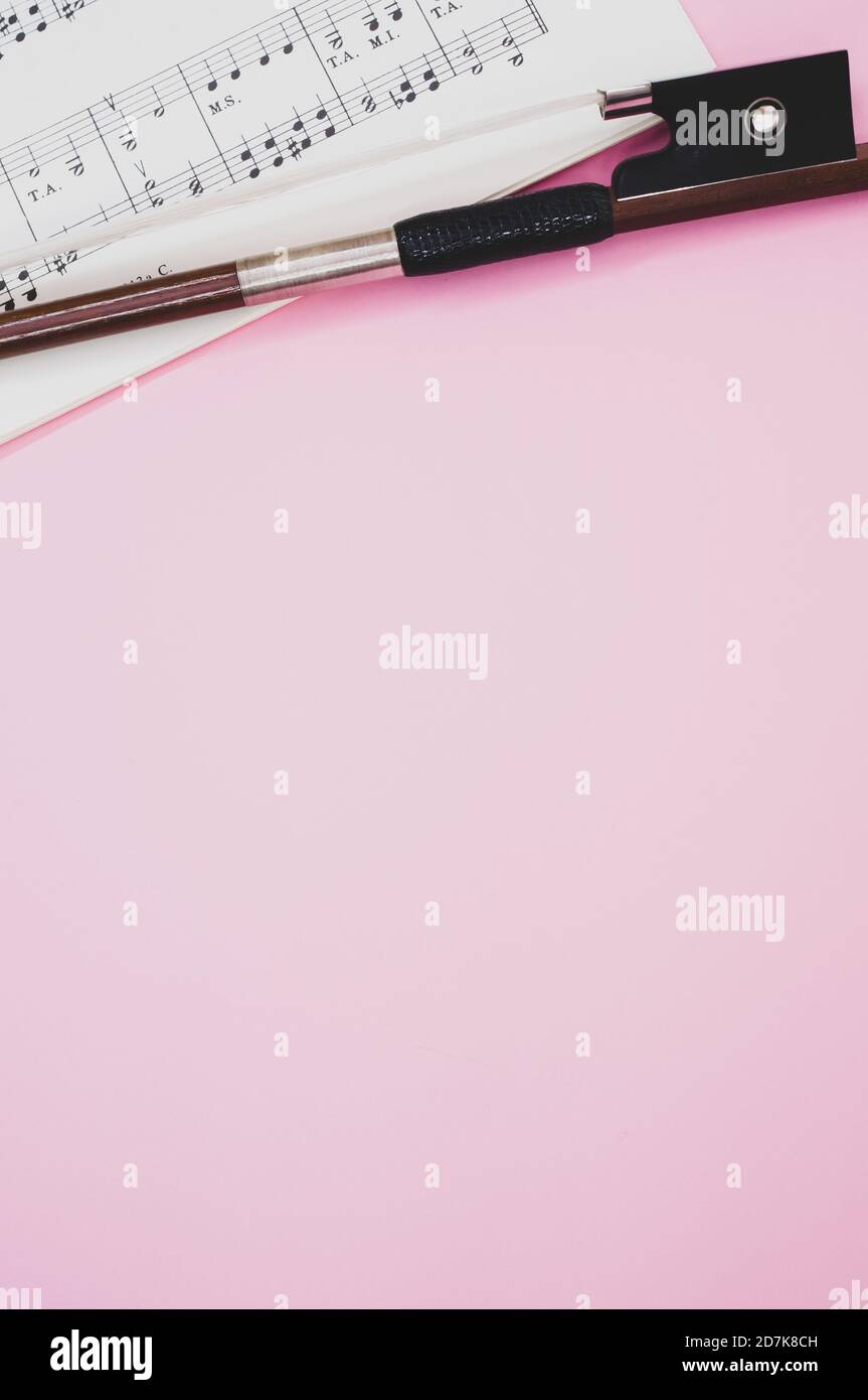 Gros plan d'un arc de violon avec partitions sur le surface rose - espace pour le texte Banque D'Images