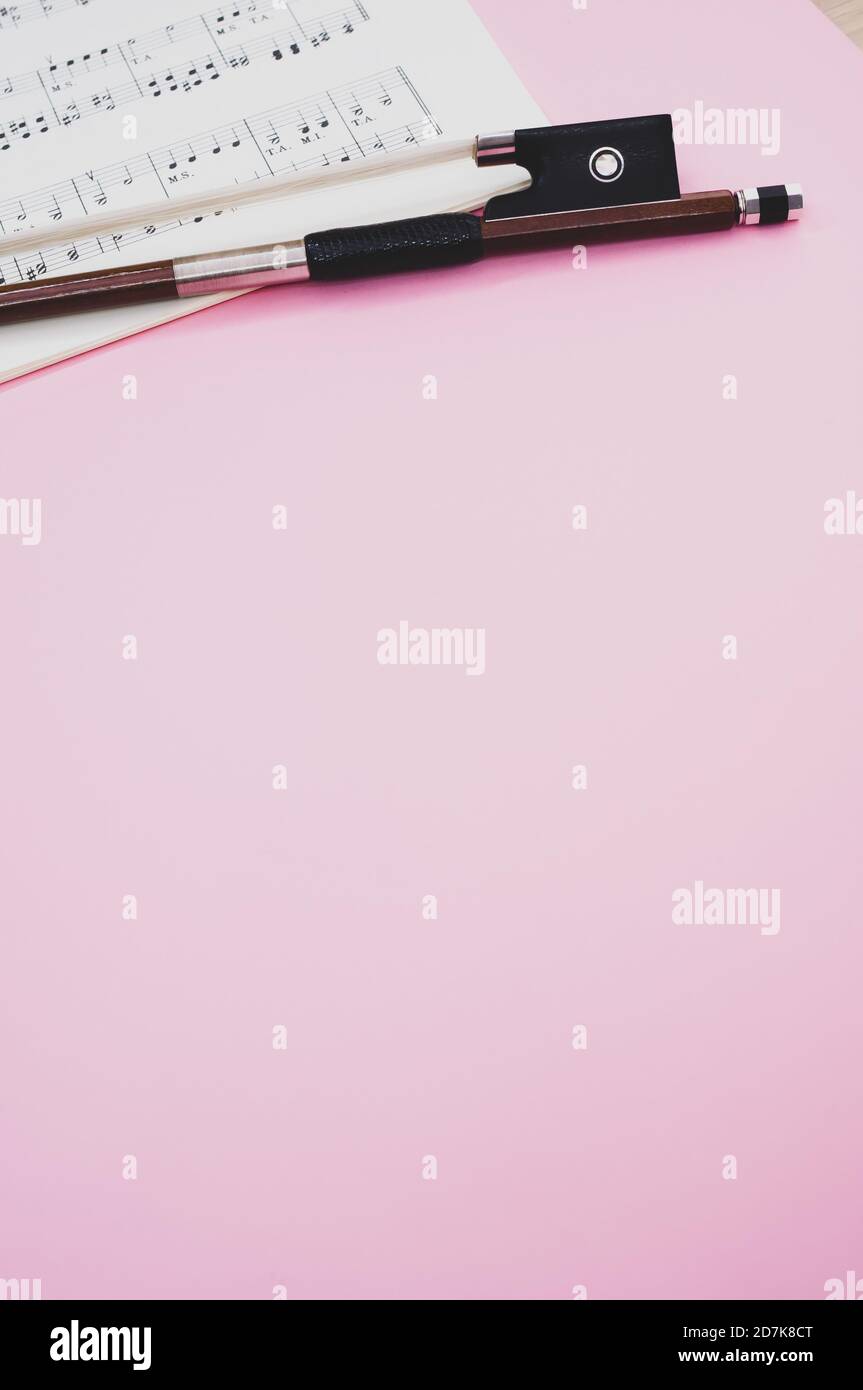 Gros plan d'un arc de violon avec partitions sur le surface rose - espace pour le texte Banque D'Images