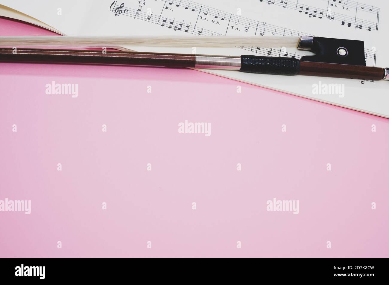 Gros plan d'un arc de violon avec partitions sur le surface rose Banque D'Images
