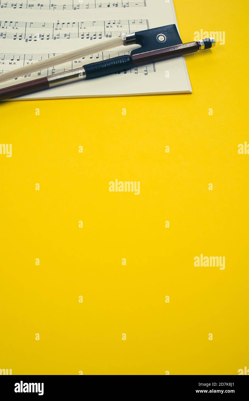 Gros plan d'un arc de violon avec partitions sur le surface jaune - espace pour le texte Banque D'Images