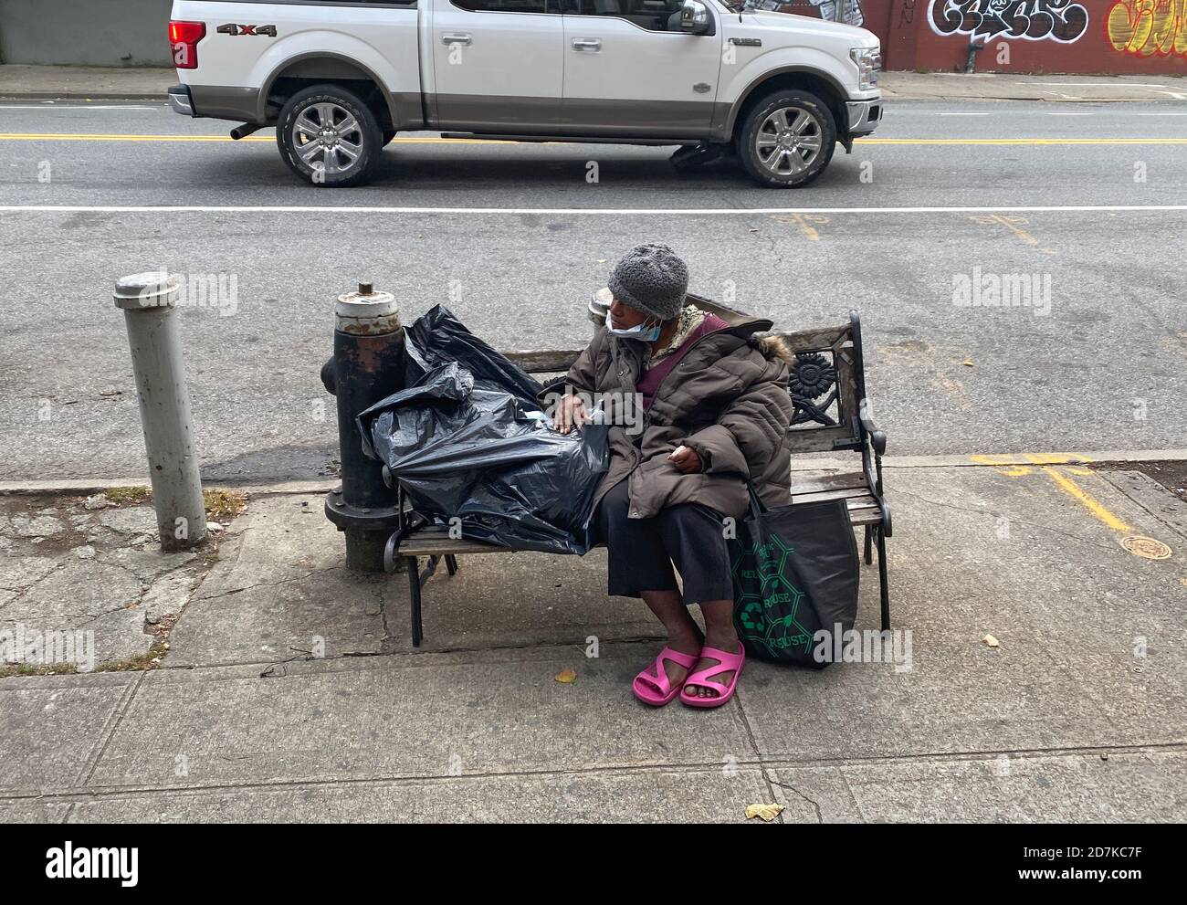 Une femme âgée sans abri est assise sur un banc sur Church Avenue dans le quartier de Kensington à Brooklyn, New York. Banque D'Images