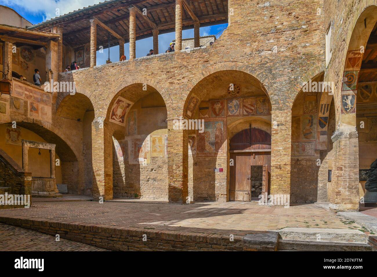 Cour de l'hôtel de ville du Palazzo Comunale avec des touristes alignés sous la verrière pour entrer dans le Musée civique, San Gimignano, Sienne, Toscane, Italie Banque D'Images
