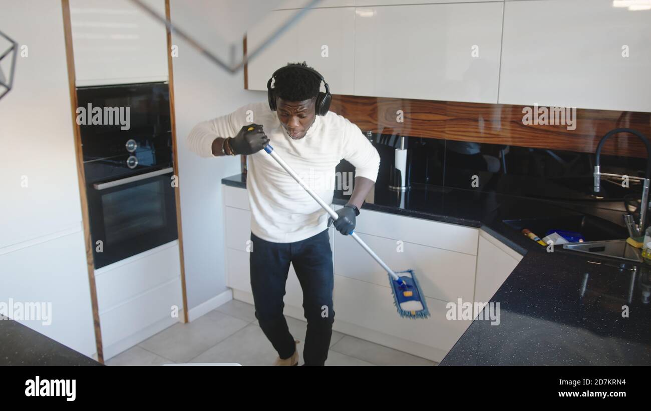 Joyeux homme noir beau à l'écoute de la musique et à l'utilisation du balai comme guitare. Fatiguant l'appartement. Photo de haute qualité Banque D'Images