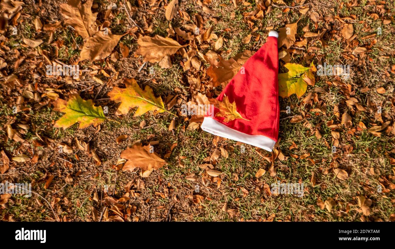 Noël et l'hiver arrivent bientôt. Une photo de fond conceptuelle du chapeau du Père Noël sur les feuilles jaunes en automne. Dernier jour de vacances d'automne et d'hiver Banque D'Images