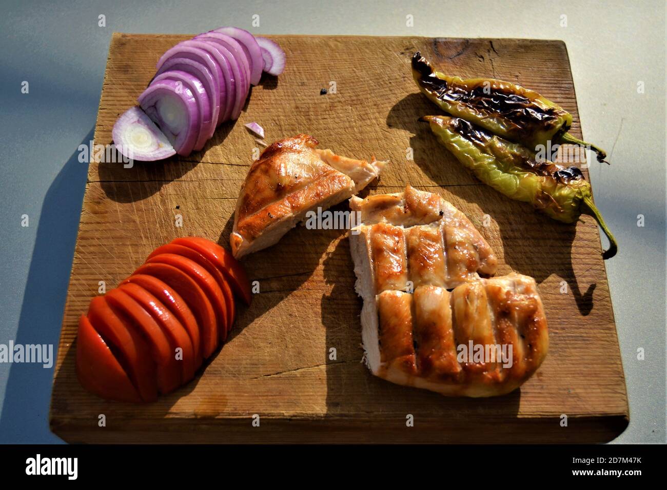 Délicieuse viande blanche cuite au moyen du gril. Poulet gril bien cuit avec tomate, oignon et poivre. Tout cela est indiqué sur une plaque en bois. Banque D'Images