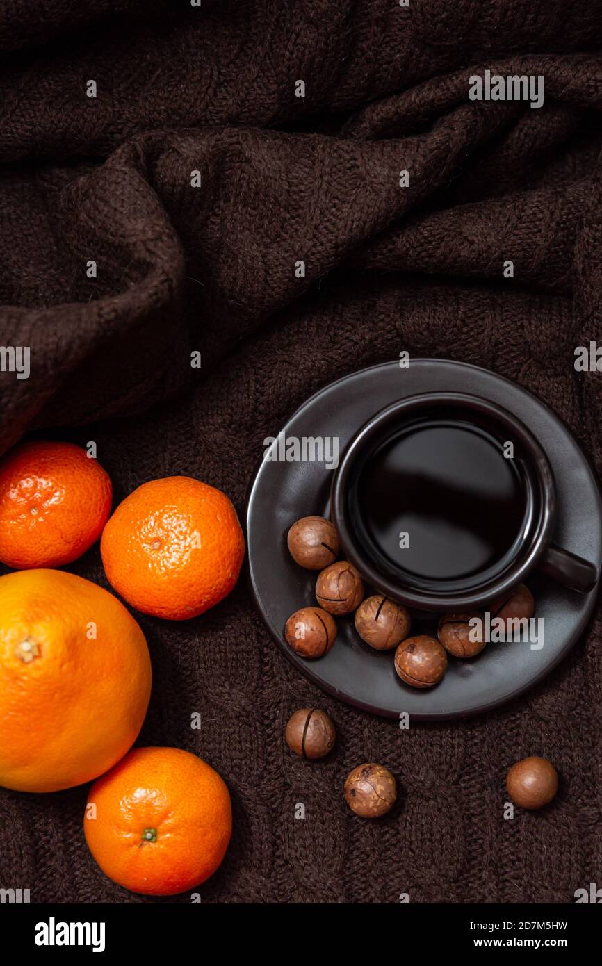 Ambiance chaleureuse. Tasse de café avec mandarines et noix sur fond de couverture tricotée marron Banque D'Images