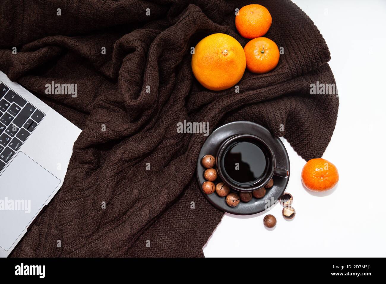 Ambiance chaleureuse. Ordinateur portable, tasse de café avec mandarines et noix sur fond de couverture tricoté marron Banque D'Images