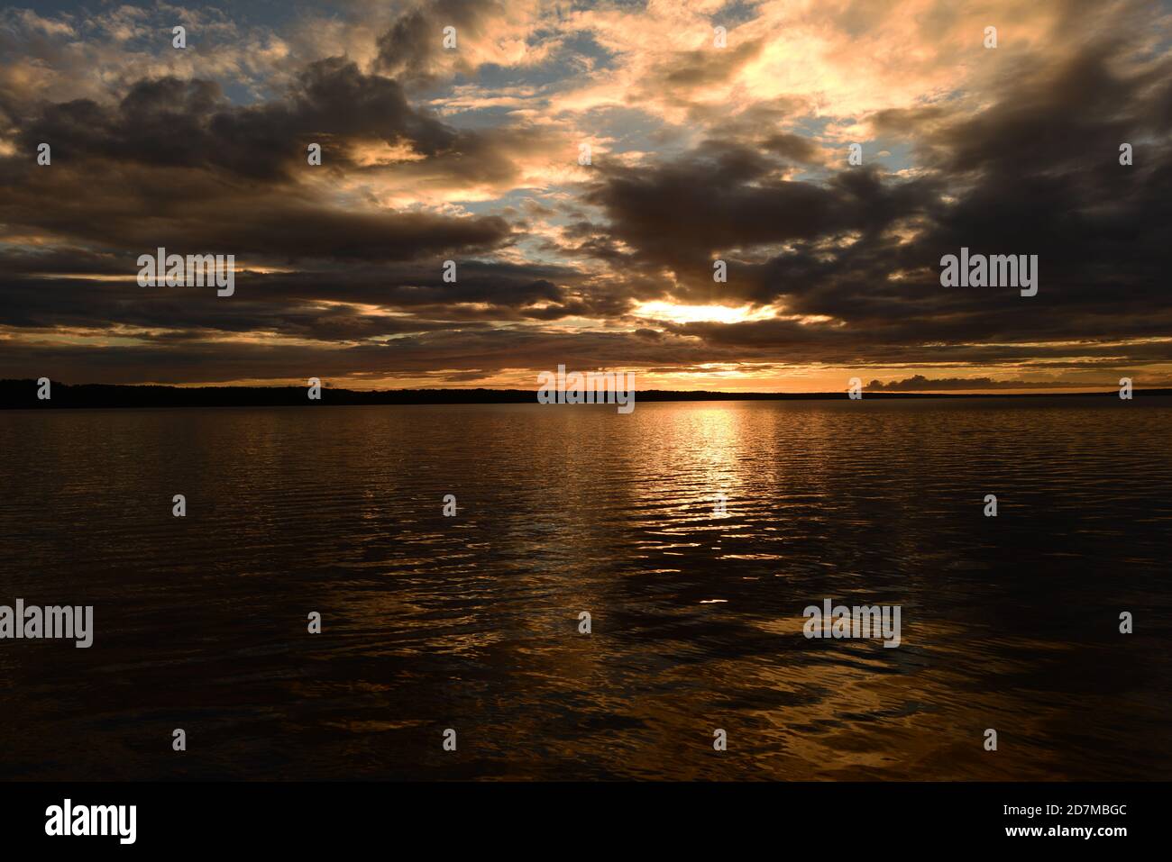 La lumière du soleil sur le ciel nuageux crépuscule est reflétée par lumière colorée et ombres sur l'eau du lac Banque D'Images