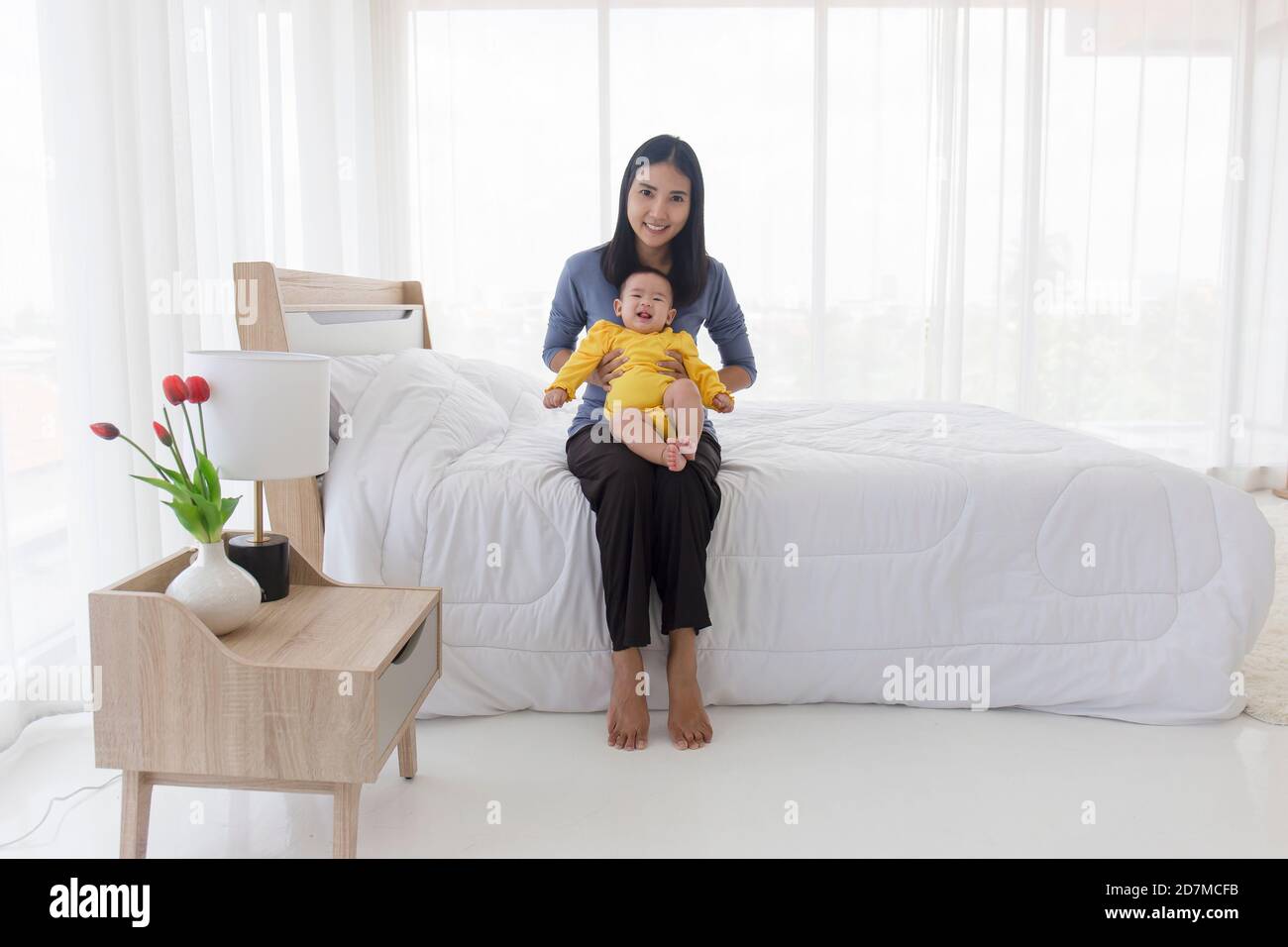Une maman asiatique joue avec plaisir avec son bébé au lit. Banque D'Images