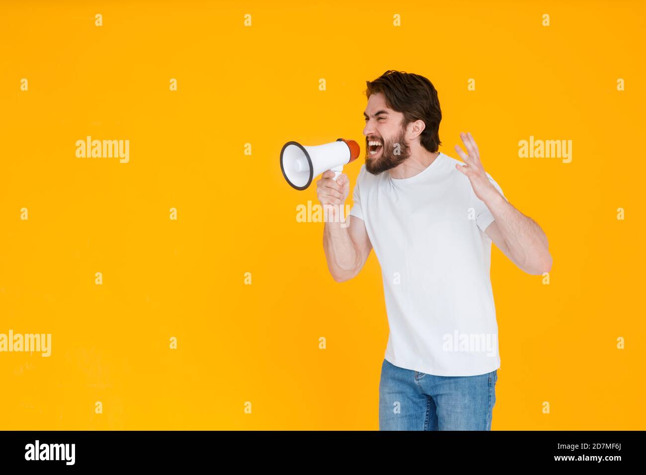Jeune homme en colère dans un t-shirt blanc posé isolé sur fond jaune orange, portrait de studio. Personnes émotions sincères concept de style de vie. Maquette Banque D'Images
