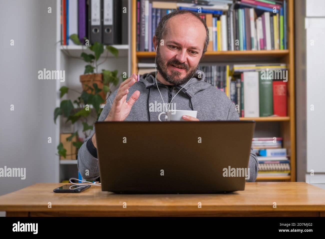 Homme travaillant en ligne depuis la maison sur un ordinateur portable derrière un bureau d'époque, avec des écouteurs, parlant et expliquant à des collègues lors d'une réunion en ligne Banque D'Images