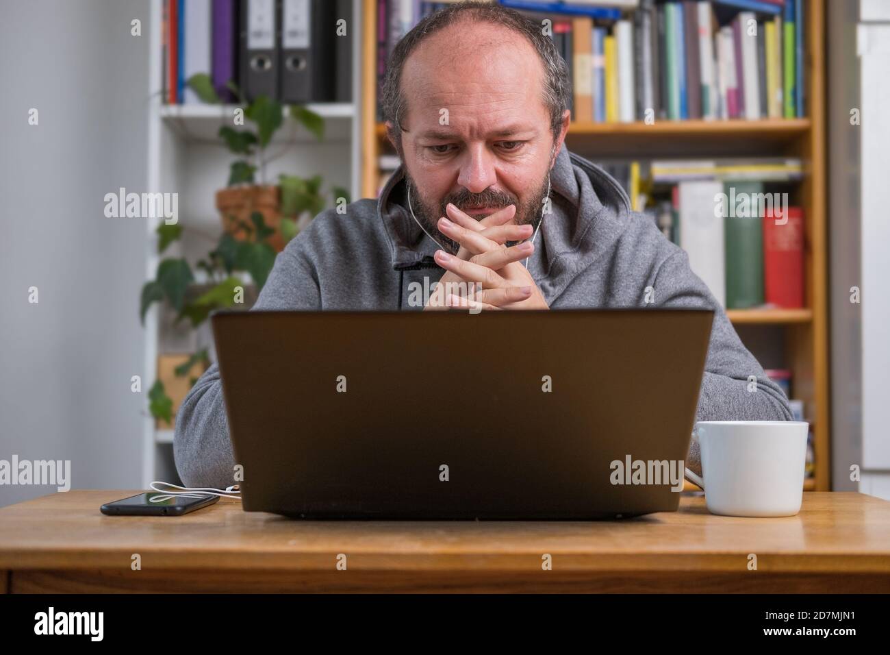 Homme travaillant en ligne depuis un bureau à domicile sur un ordinateur portable derrière un bureau d'époque, concentré, avec des écouteurs, à l'écoute de la réunion en ligne Banque D'Images
