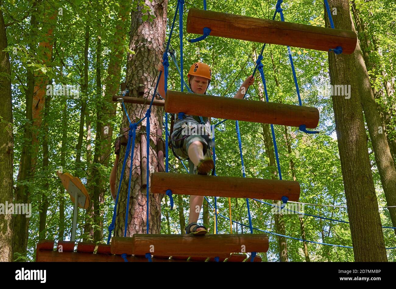 Un garçon muni d'un casque et d'une assurance passe par un parcours d'obstacles de haute altitude. Entraînement Banque D'Images