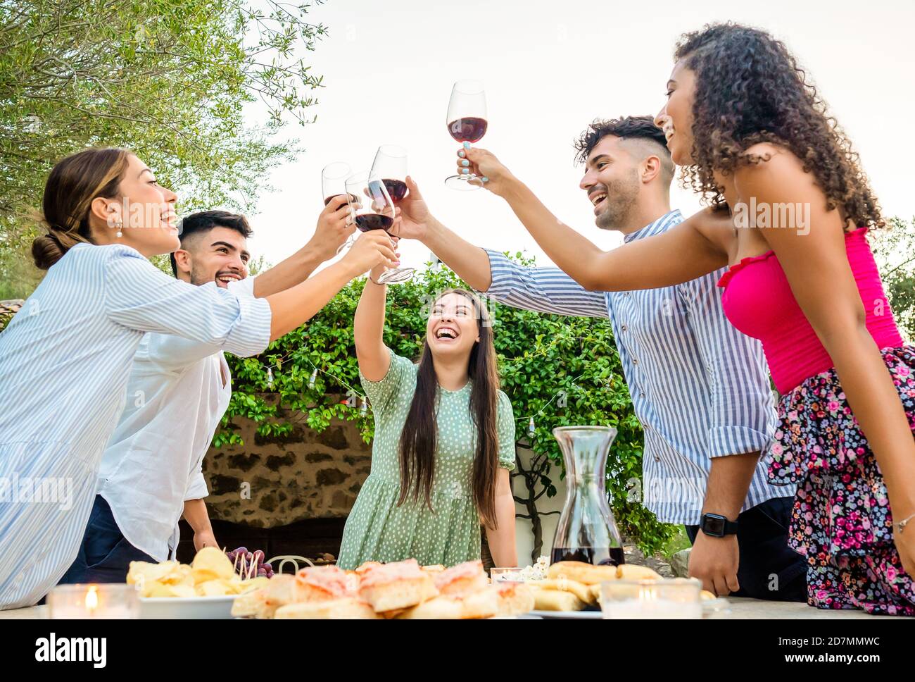 Groupe multi-ethnique de jeunes amis heureux Toaster dans le jardin Au coucher du soleil avec des verres à vin rouge - la génération y s'amuse ensemble dans la campagne de célébration Banque D'Images