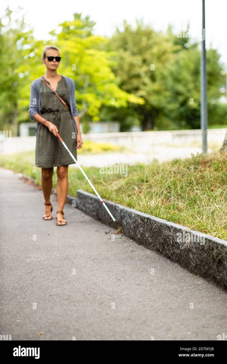 Femme aveugle marchant dans les rues de la ville, utilisant sa canne blanche pour mieux naviguer dans l'espace urbain et pour se rendre à sa destination en toute sécurité Banque D'Images