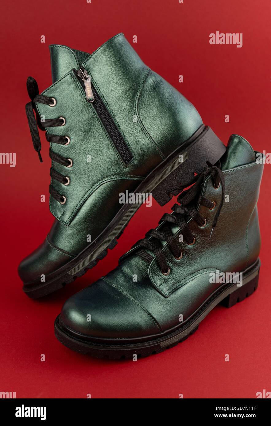 Chaussures en cuir vert. Bottes d'hiver et d'automne hors saison. Chaussure élégante isolée sur fond rouge. Gros plan. Lacets, semelle de tracteur, pour une durée de vie confortable Banque D'Images
