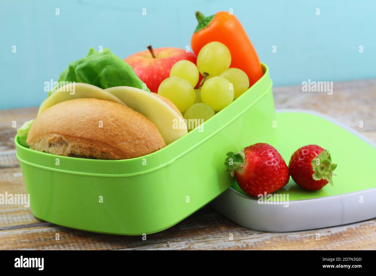 Boîte à lunch saine contenant du sandwich au fromage, du poivre jaune croquant et des fruits frais : pomme, fraises et raisins Banque D'Images