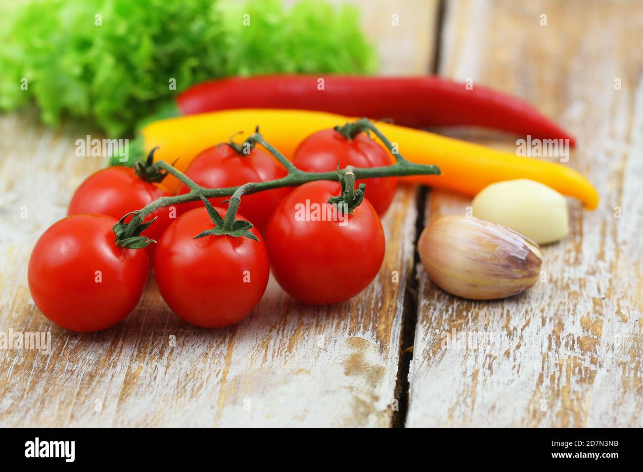 Sélection d'ingrédients de cuisson : tomates cerises, gousses d'ail et piments sur une surface en bois Banque D'Images