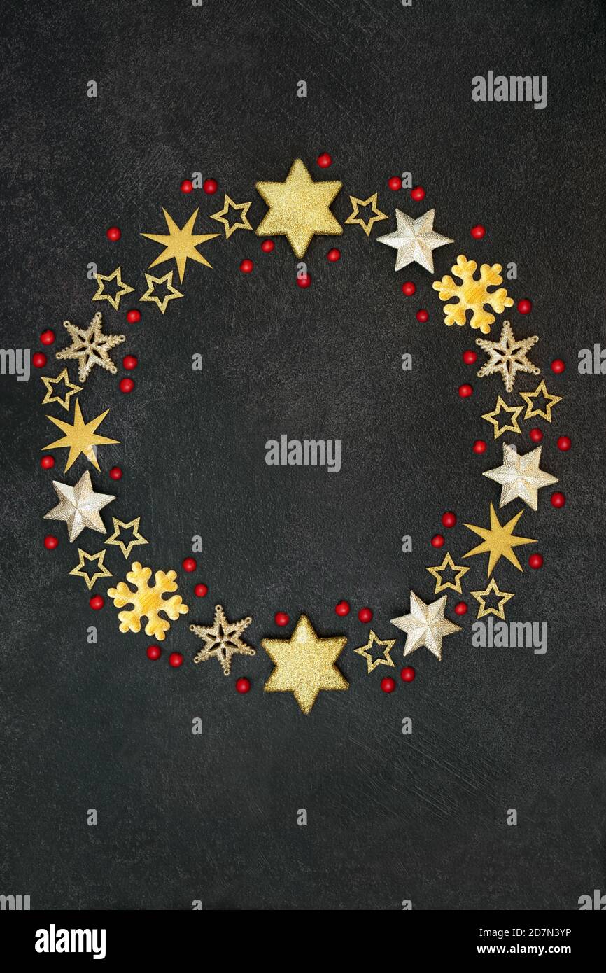 Couronne de Noël en forme de flocon de neige doré et d'étoiles avec baies de houx en vrac sur fond gris foncé. Composition abstraite pour les fêtes. Banque D'Images