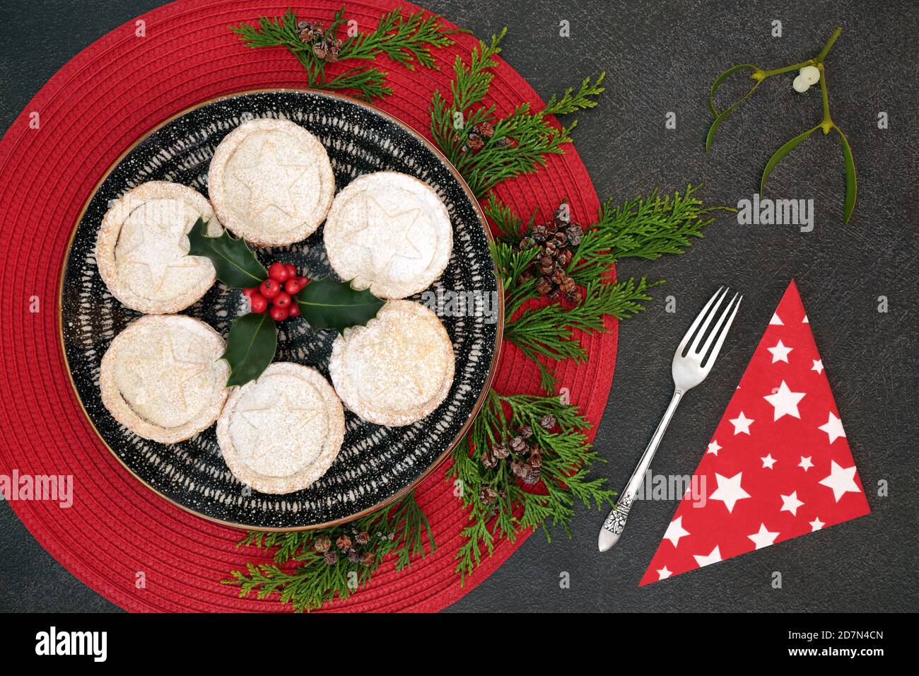 Tartes de Noël faites maison avec sapin cyprès de cèdre, houx aux baies d'hiver, fourchette d'argent antique et serviette avec branche de GUI sur fond de grunge gris. Banque D'Images