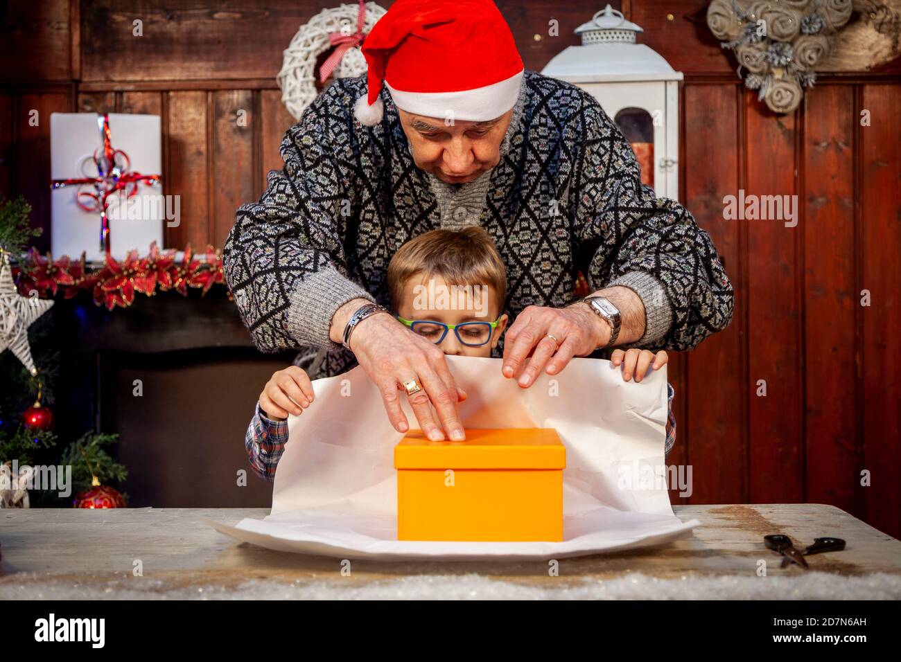 le grand-père heureux enseigne à son petit-fils comment envelopper noël cadeaux sur la table Banque D'Images