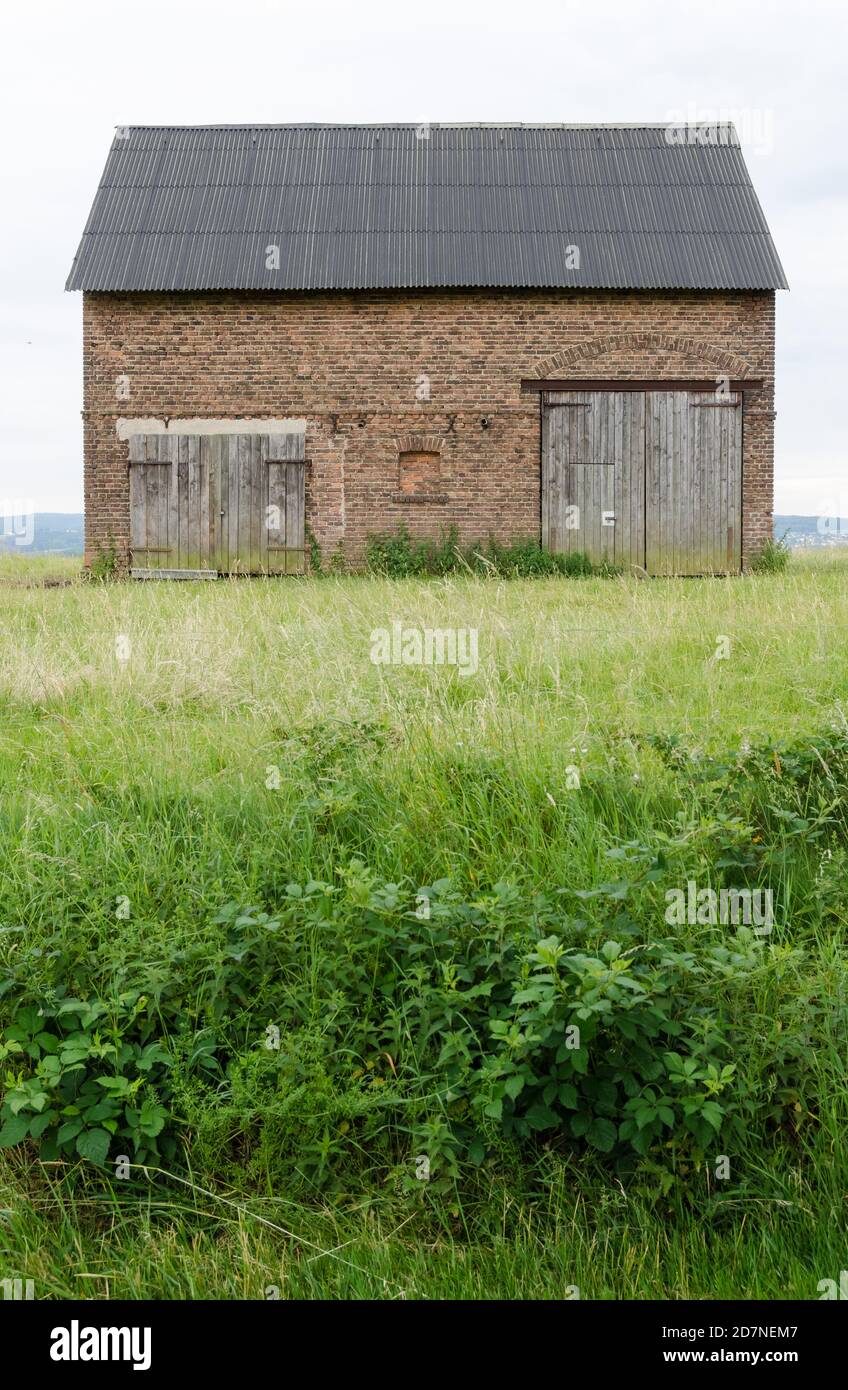 Grange abandonnée faite de briques rouges avec des portes en bois dans un champ agricole d'herbe la campagne rurale, Allemagne, Europe occidentale Banque D'Images