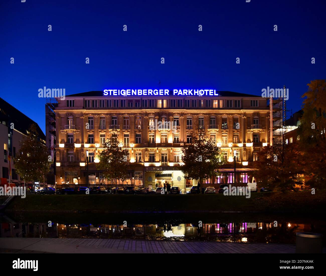 Vue extérieure de l'hôtel de luxe éclairé 'Steigenberger Parkhotel' (construit en 1902) la nuit avec ciel bleu nocturne et arbres de Noël devant. Banque D'Images