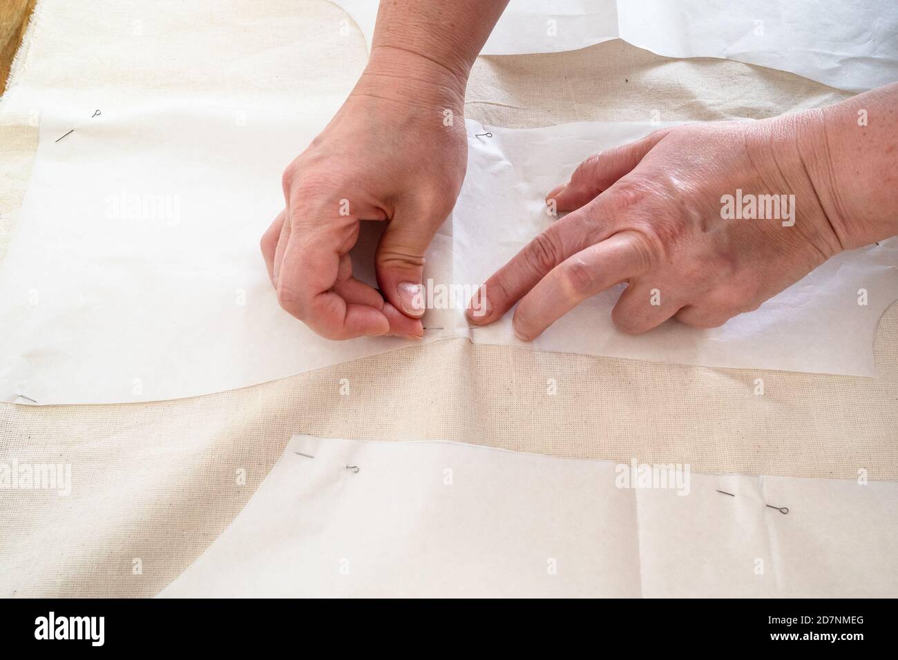 la main des tailleurs fixe les dispositions de coupe de papier de la robe à calico tissu avec épingles sur une table en bois à la maison Banque D'Images