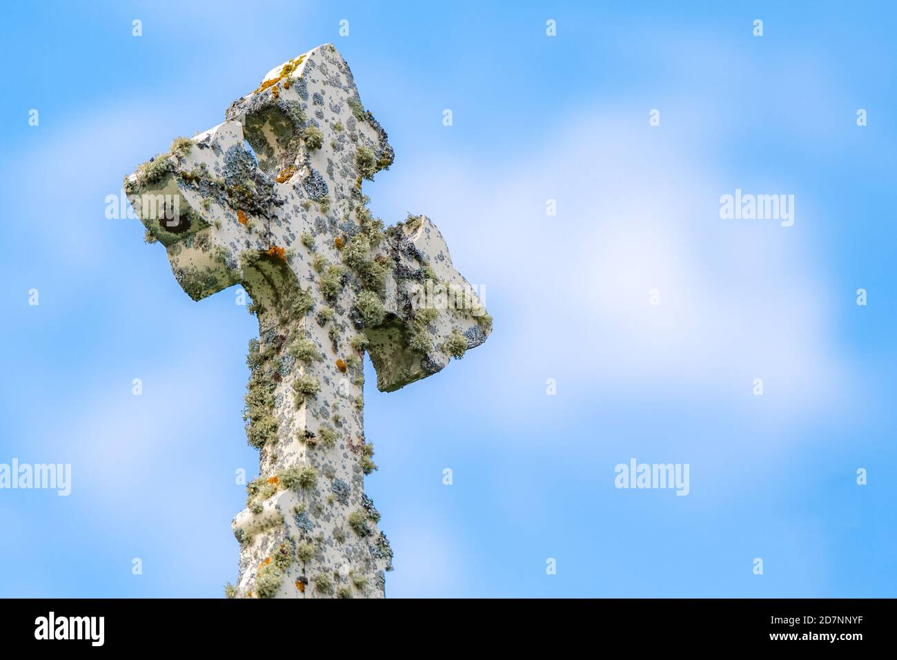 Vue sur une croix de pierre blanche de fantaisie recouverte de mousse et de lichen. Partiellement nuageux bleu timide ci-dessus. Banque D'Images